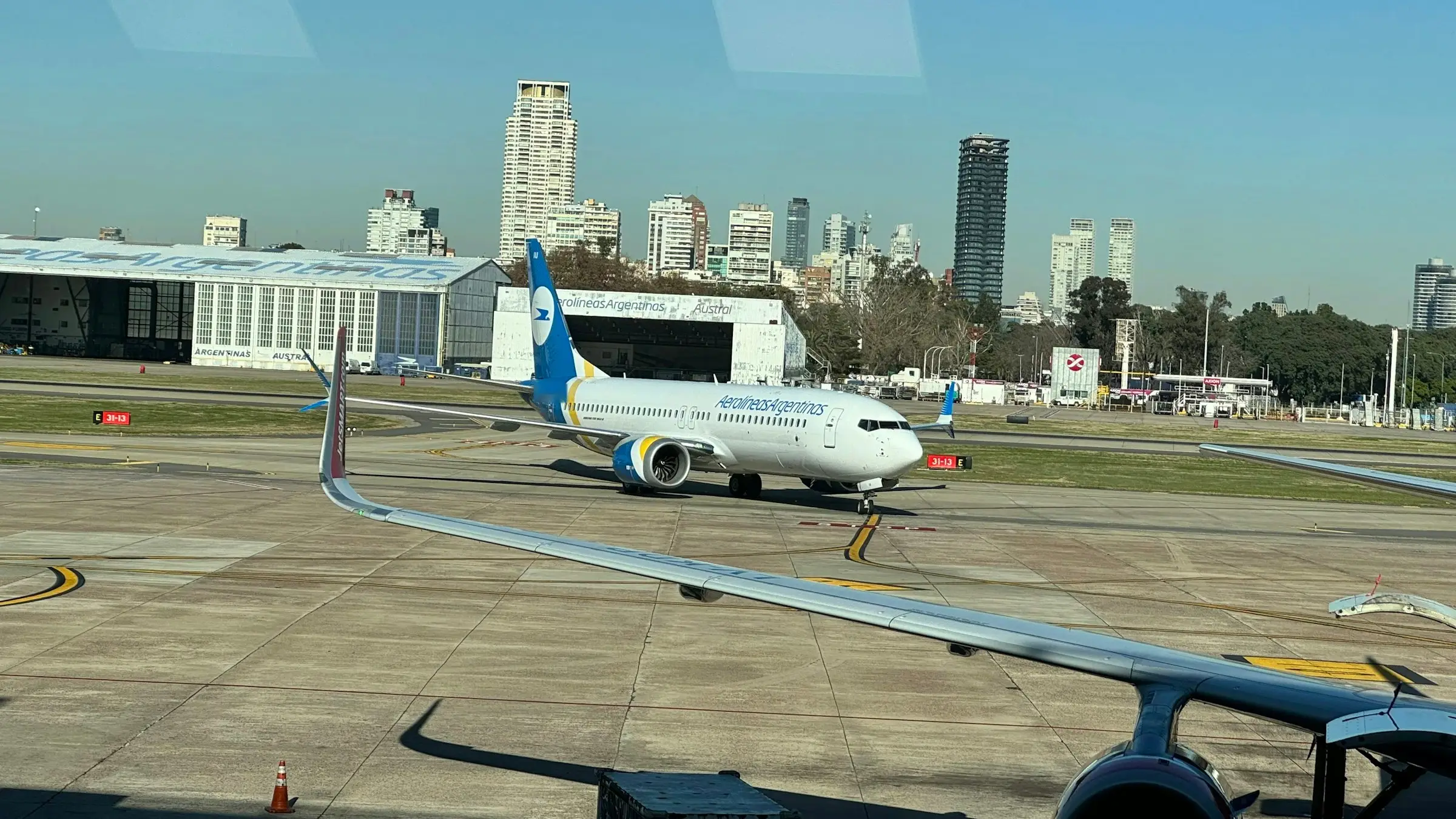 Avião comercial taxiando no pátio do Aeroparque com hangares e os prédios de Buenos Aires ao fundo