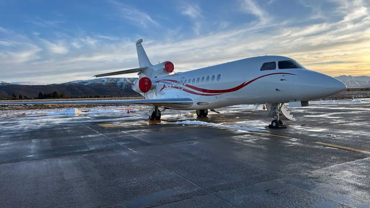 Falcon business jet on the snow-dusted Bariloche apron at sunset, with the mountains behind