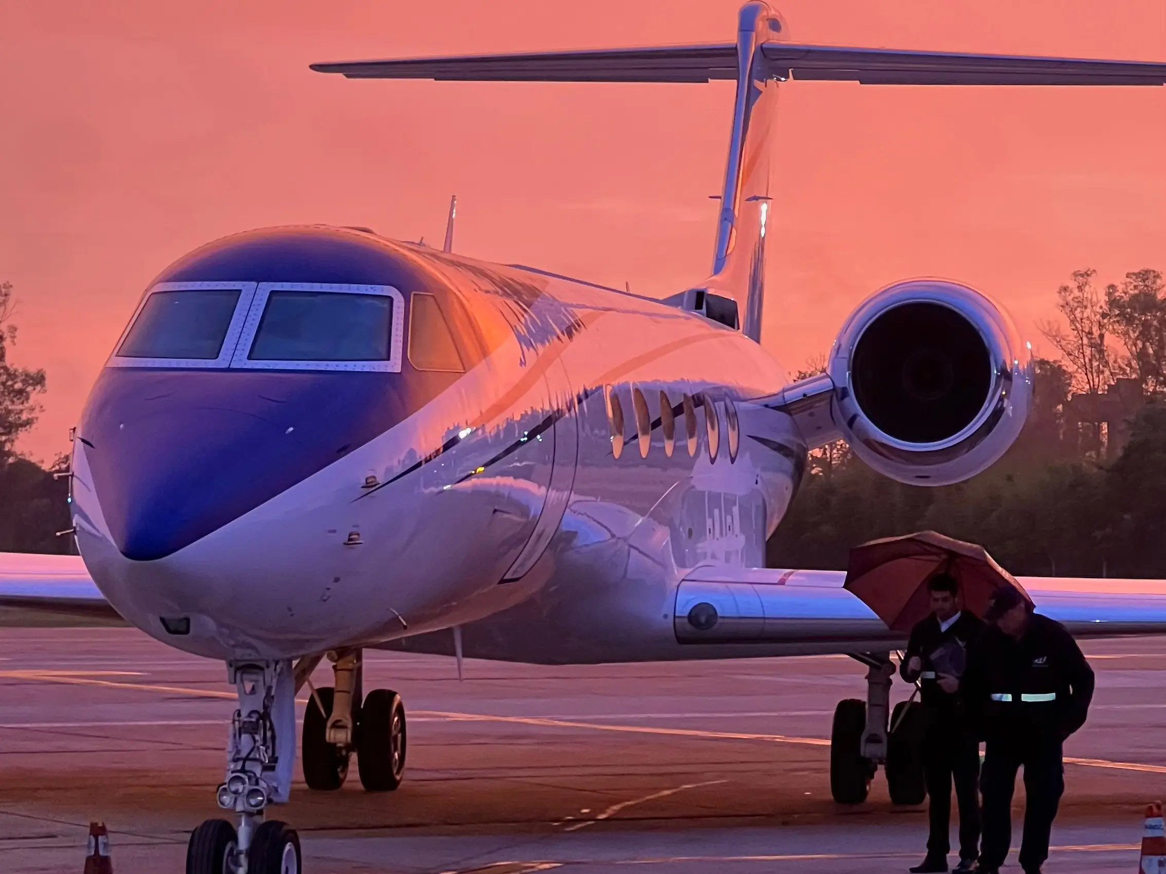 Large-cabin business jet at twilight on the Ezeiza apron, with ground crew under an umbrella