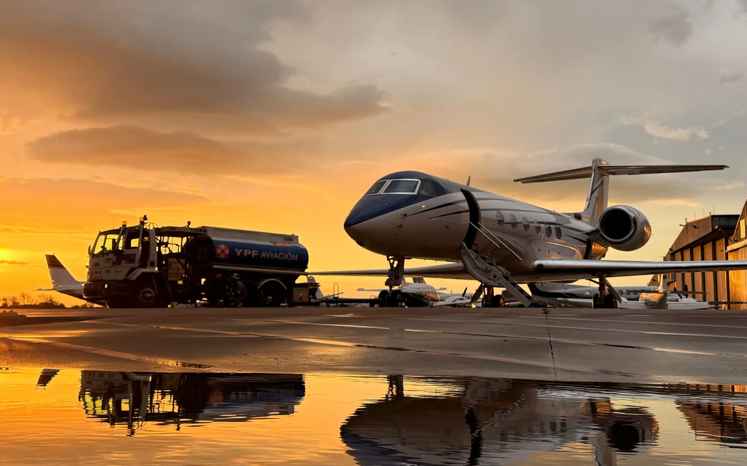 Large-cabin business jet and fuel truck at sunset on the San Fernando apron, reflected on the wet ramp