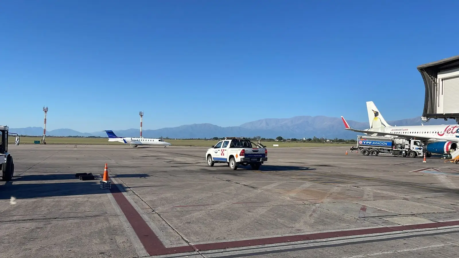 Light business jet taxiing on the Salta apron, with the jet bridge and the mountains behind