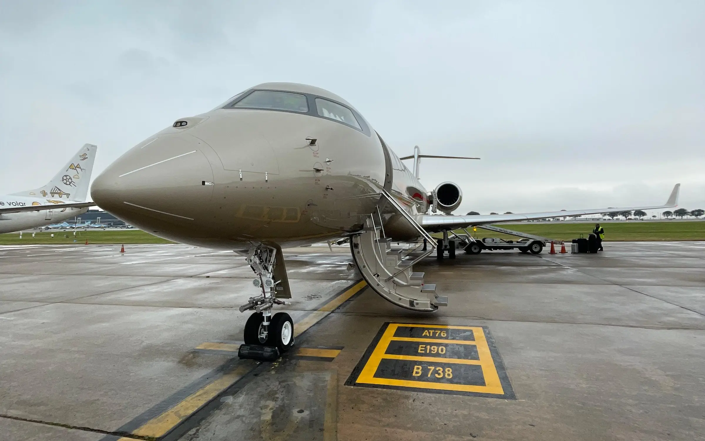 Champagne-colored long-range business jet with its airstair down on the wet Aeroparque apron