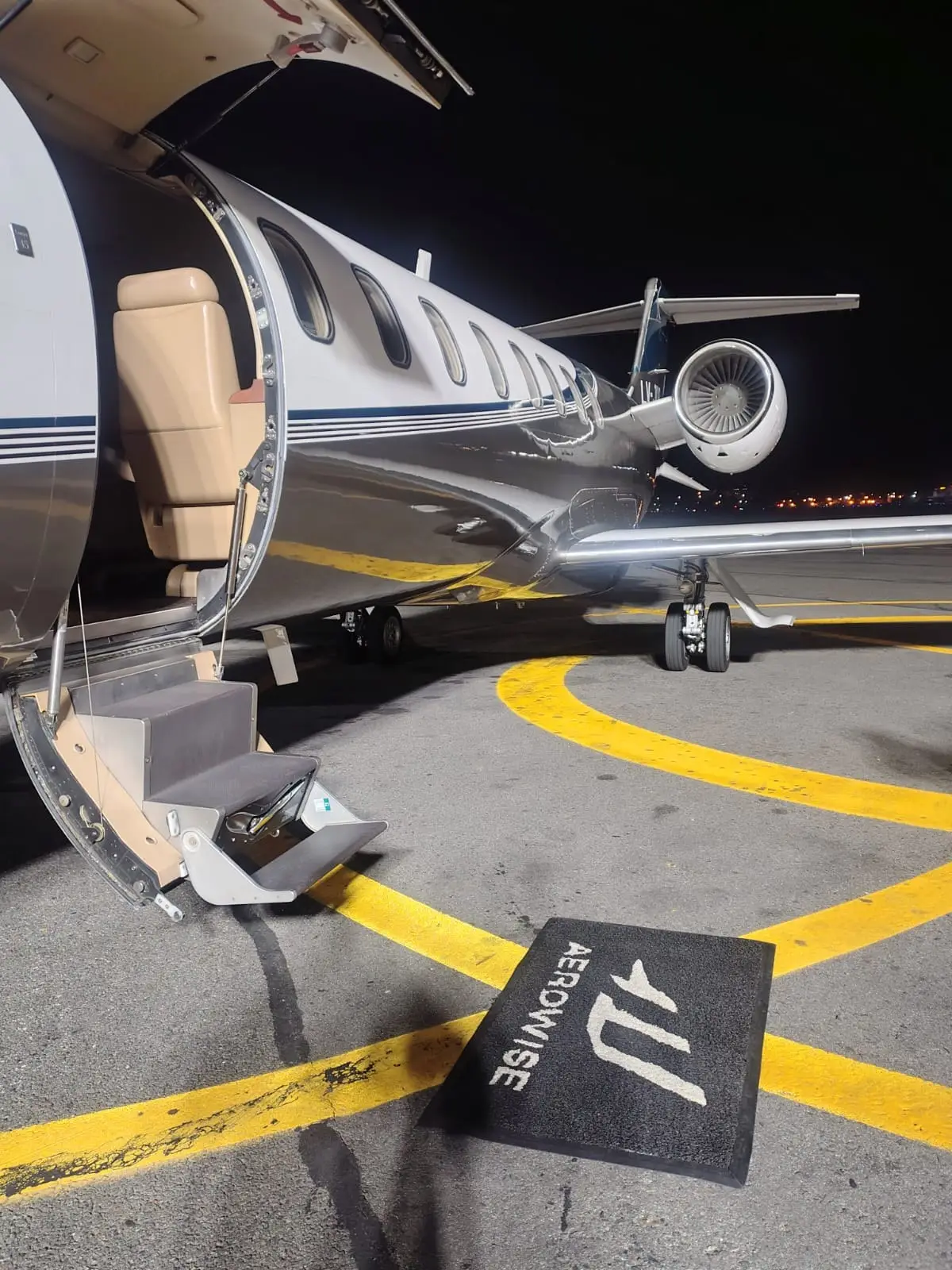 Business jet with its airstair down next to an Aerowise mat on the apron at night